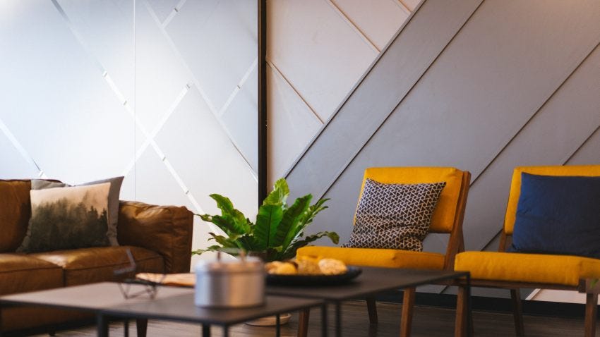 Casual office setting with two yellow chairs with throw pillows, a brown leather couch and a coffee table with plants.