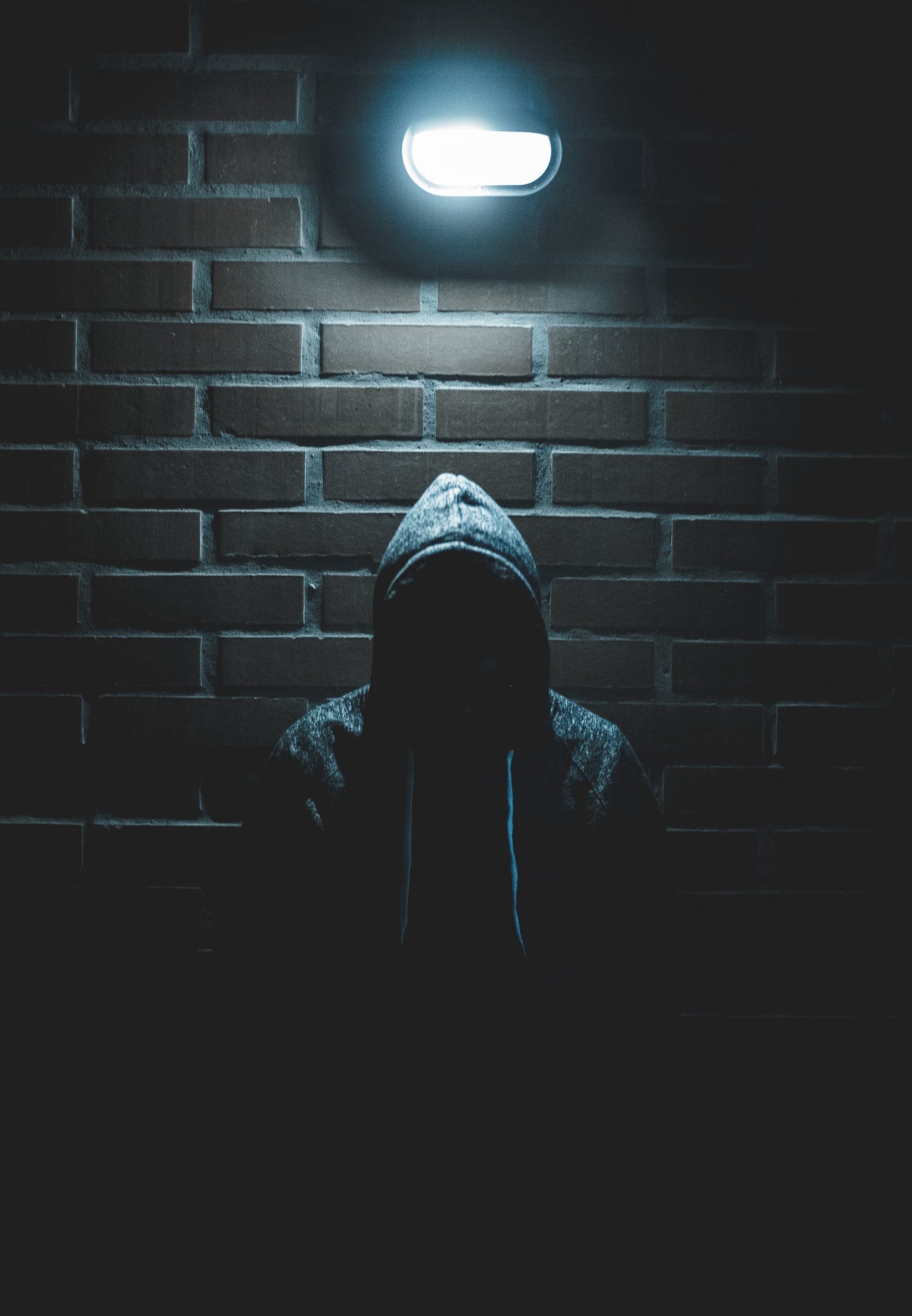 Hooded figure against a brick wall.