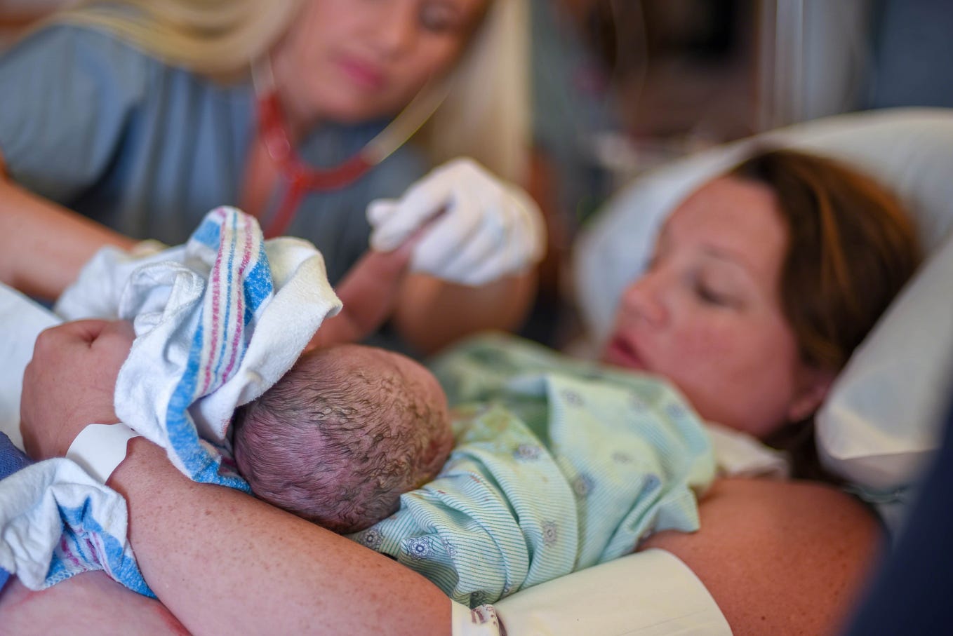 Woman holding newborn baby with midwife by her side.