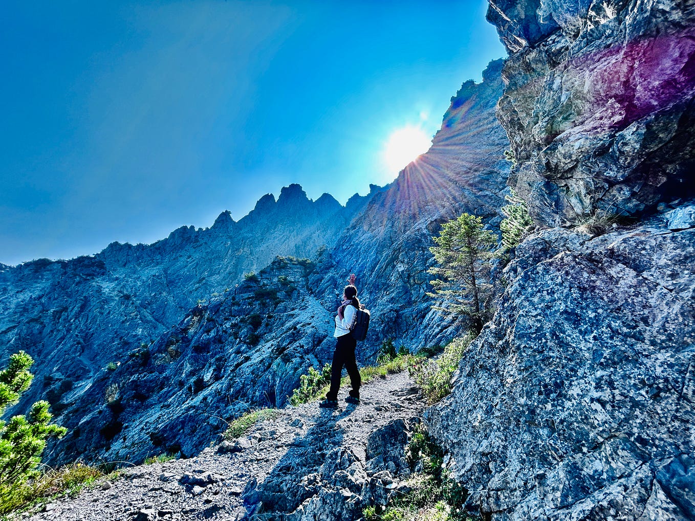 a mountain rocks with a sun shining on top of the rocks and a blue sky with the woman standing on the rocks