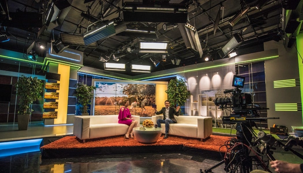 wide shot of television talk show. TV camera and stage lights visible as well as hosts on set.