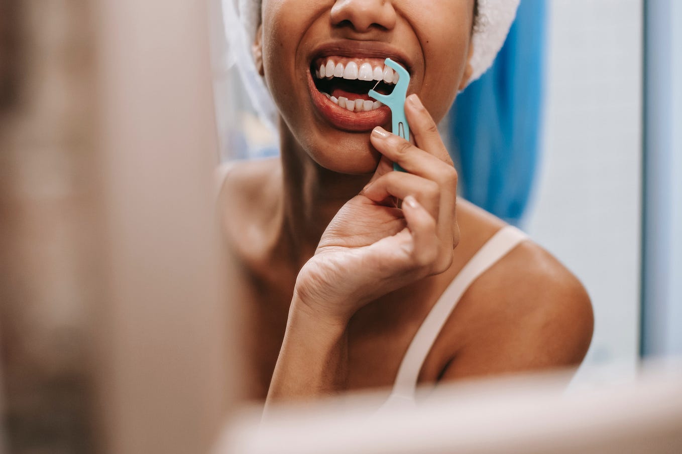 Woman in a bathroom mirror using a tooth flosser.