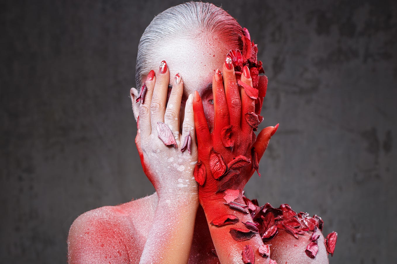 Headshot of a woman with her hands covering her face. She is spray-painted white on one side and red on the other. There are also leaves clinging to her. They too are spray painted.