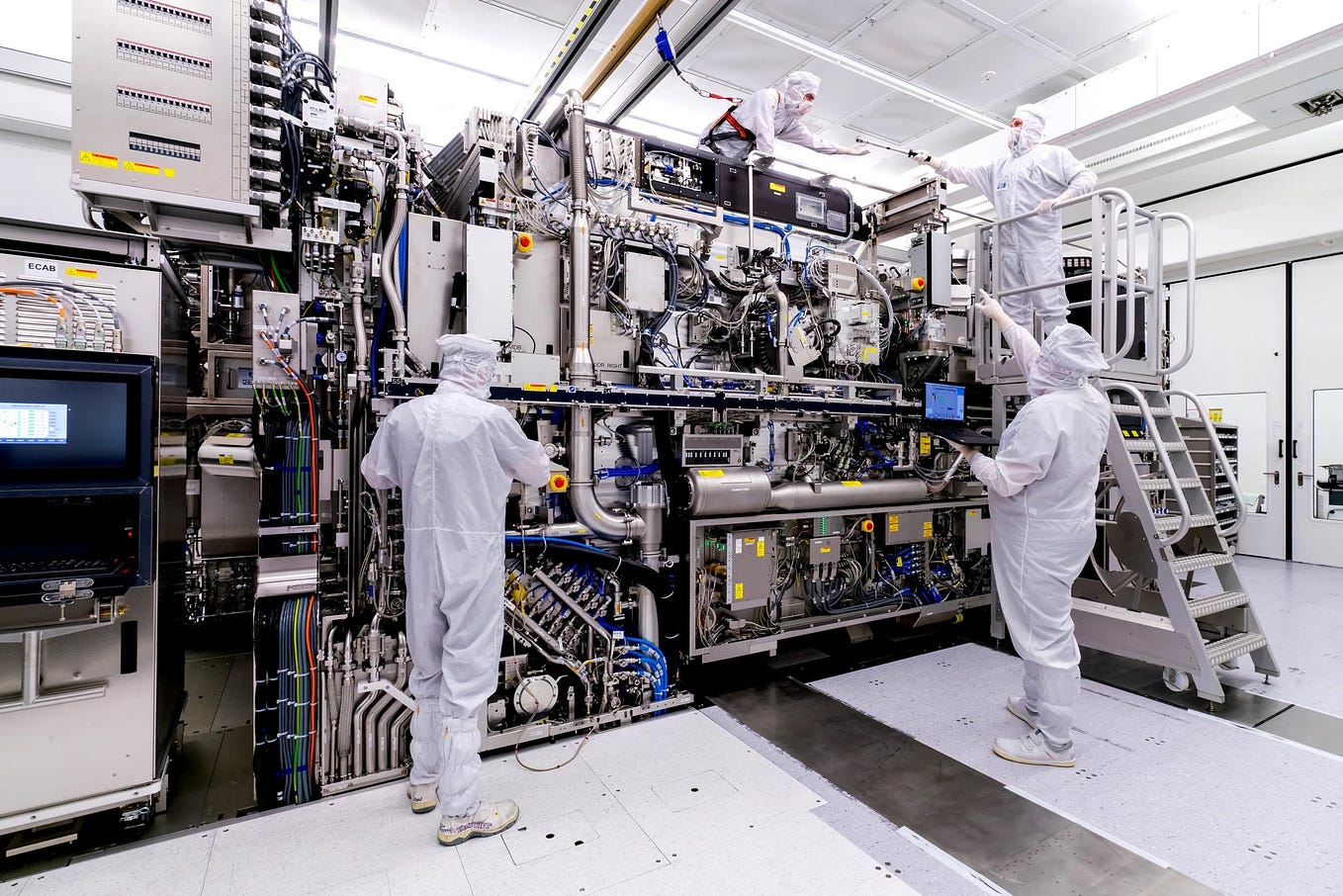 Four people constructing an immensely complicated machine. They are wearing white body suits to prevent dust from getting into the machine.