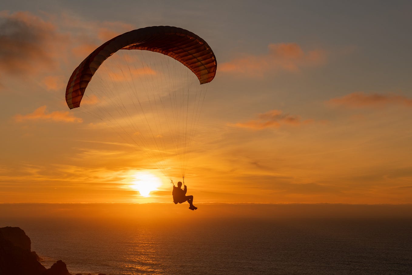 A man paragliding over a sea at sunset