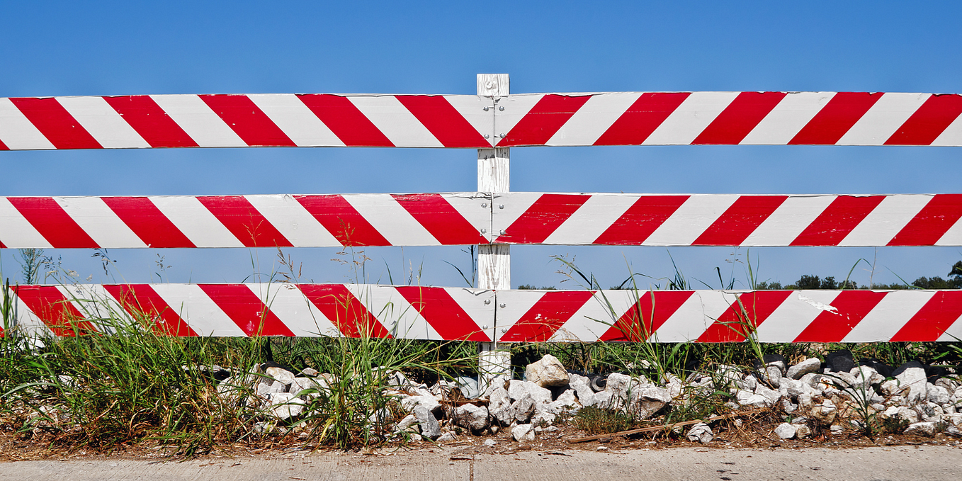Photo of a red and white striped traffic barrier with blue sky in the background.