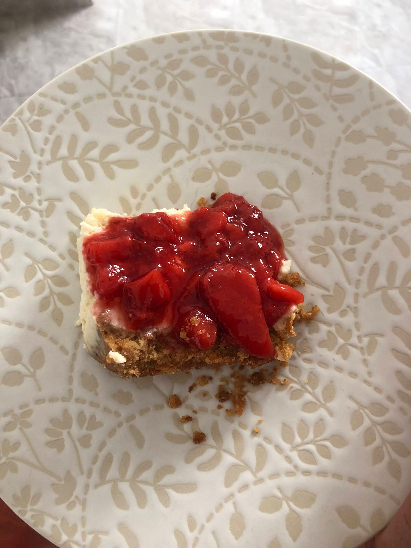 a slice of strawberry cheesecake with a strawberry compote on a floral patterned plate.
