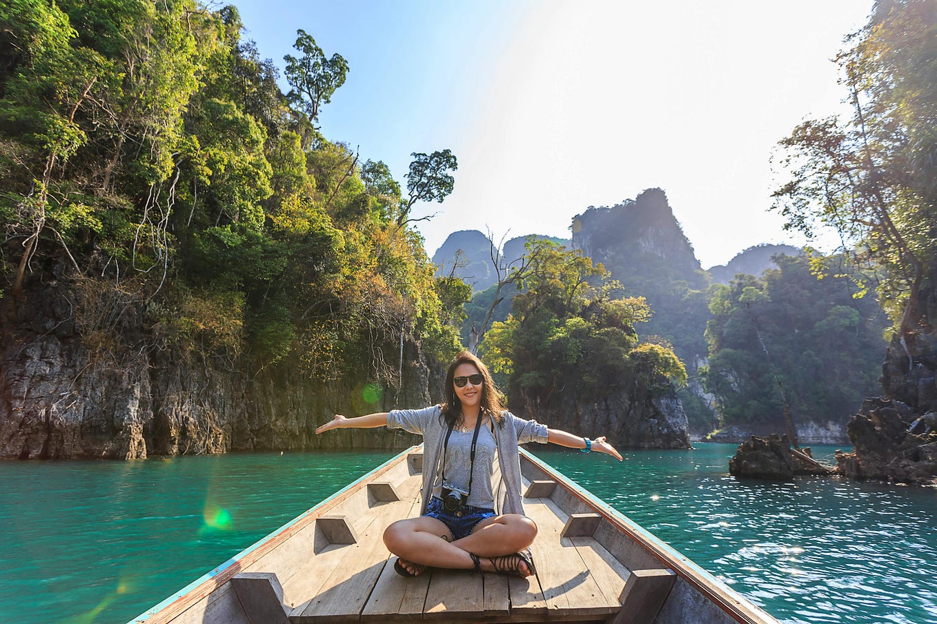 Woman sitting on a wooden walkway across a beautiful clear blue lake, surrounded by trees and rocky hillsides