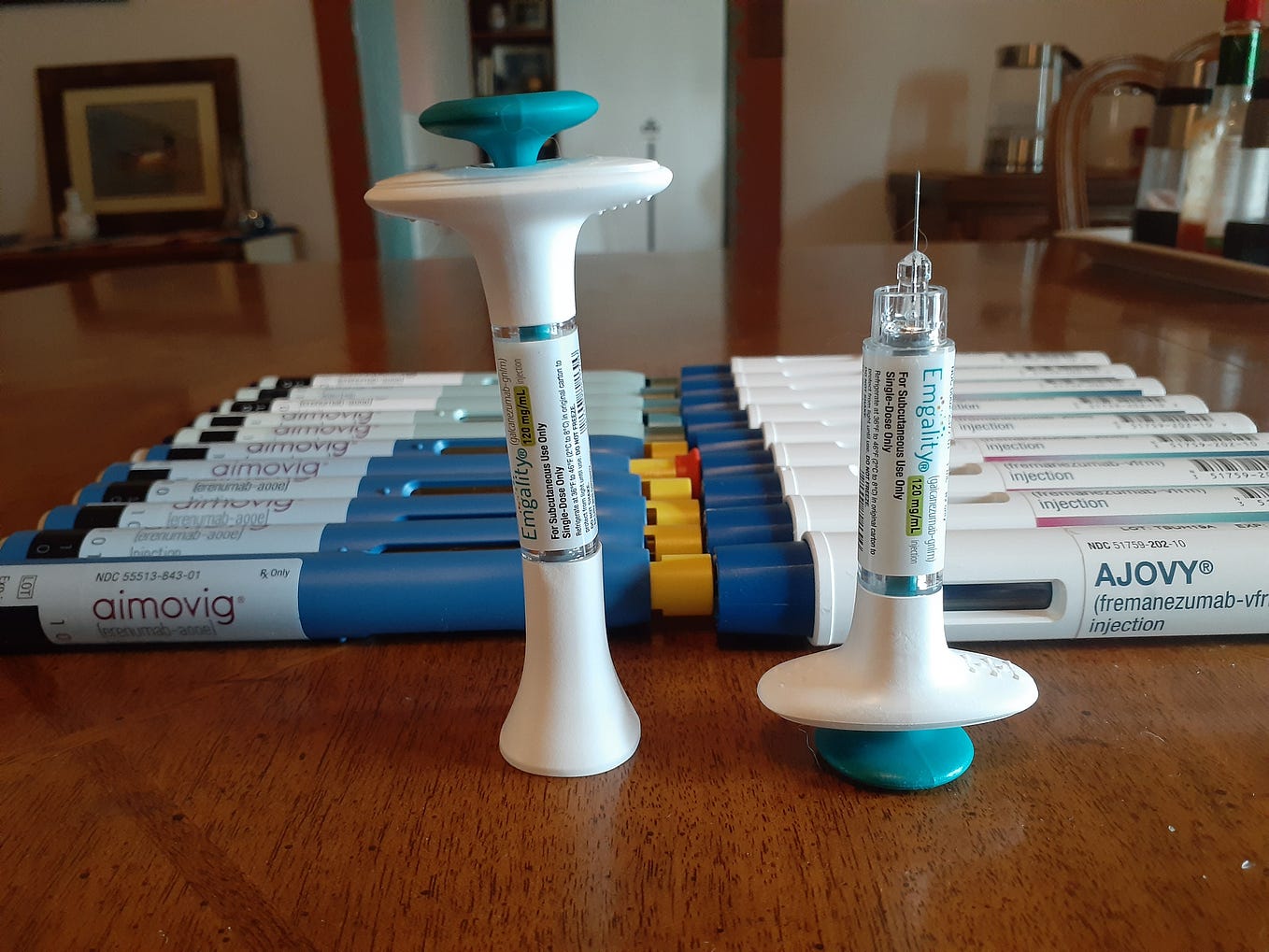 20+ autoinjectors fronted by two prefilled syringes on a dining room table.