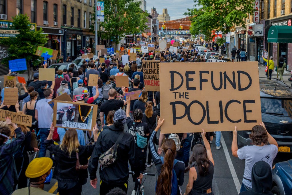 A photo of a protest. One big sign reads “DEFUND THE POLICE.”