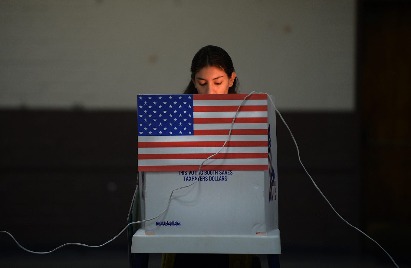 Latina woman voting at a poll in California. The booth has an American flag on it.