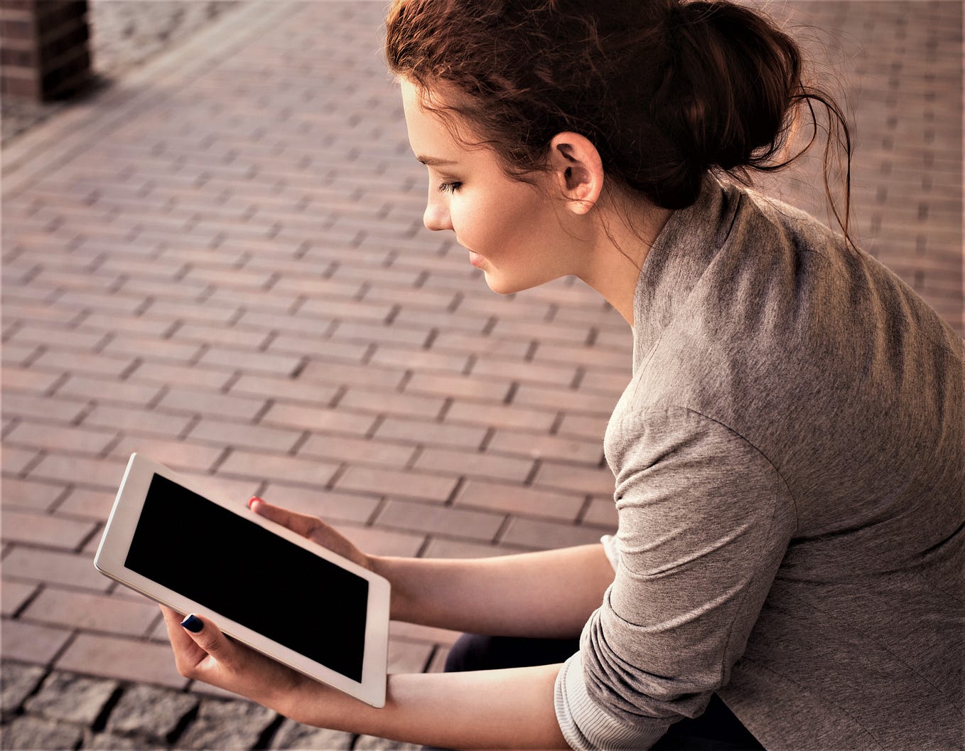 girl with brown hair gathered up on her head wearing light tan shirt and holding tablet