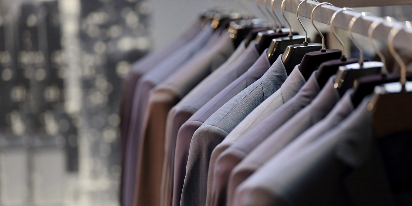 Several suits in slightly varying shades of gray hang on a rack.
