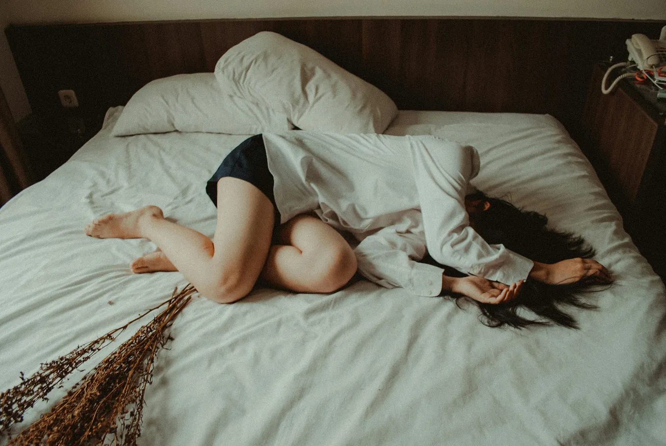 Girl curled up on an unmade bed with her arms over her face.