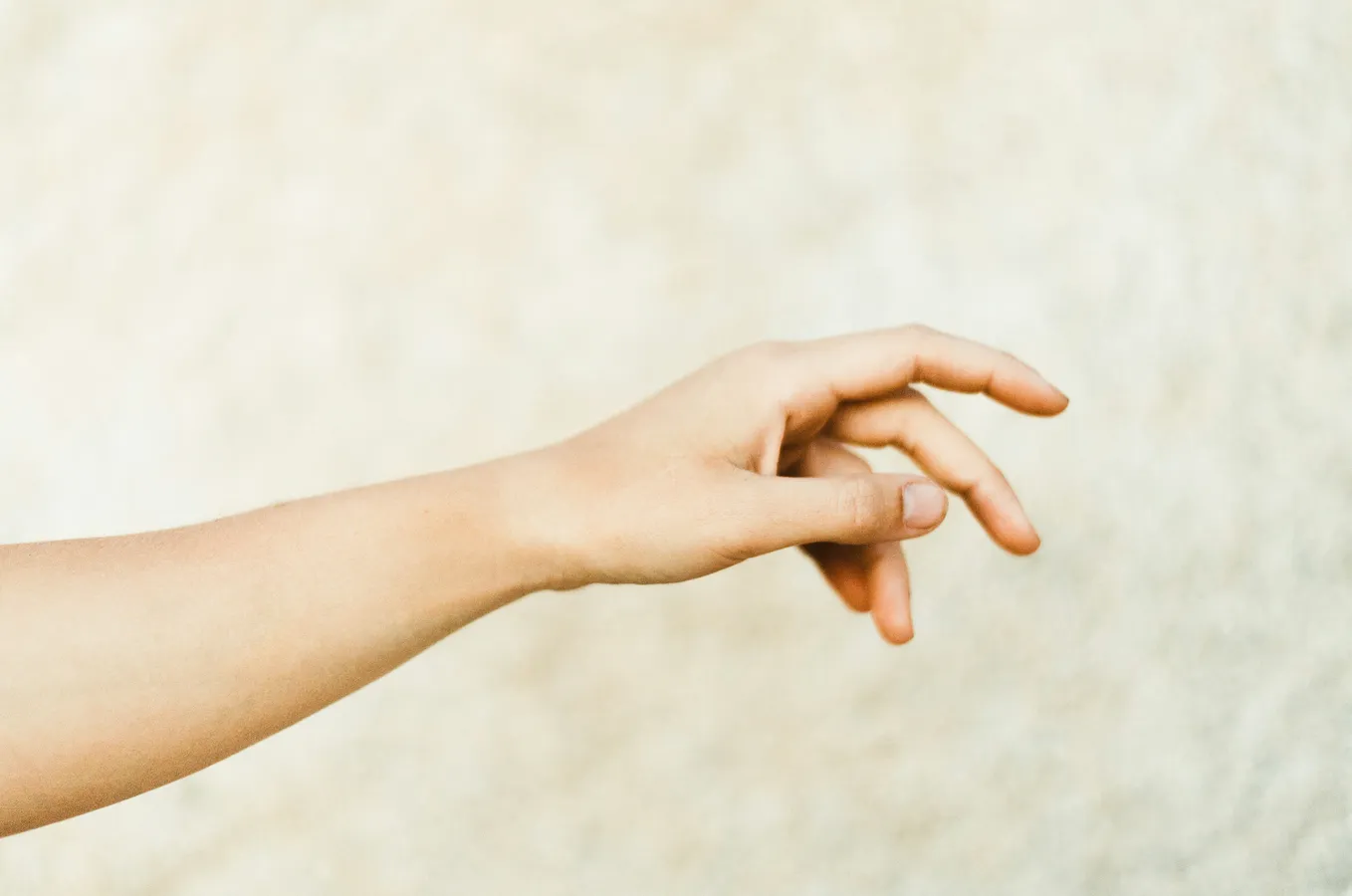 An extended human arm performing a simple hand gesture mid air against a light beige and textured background.