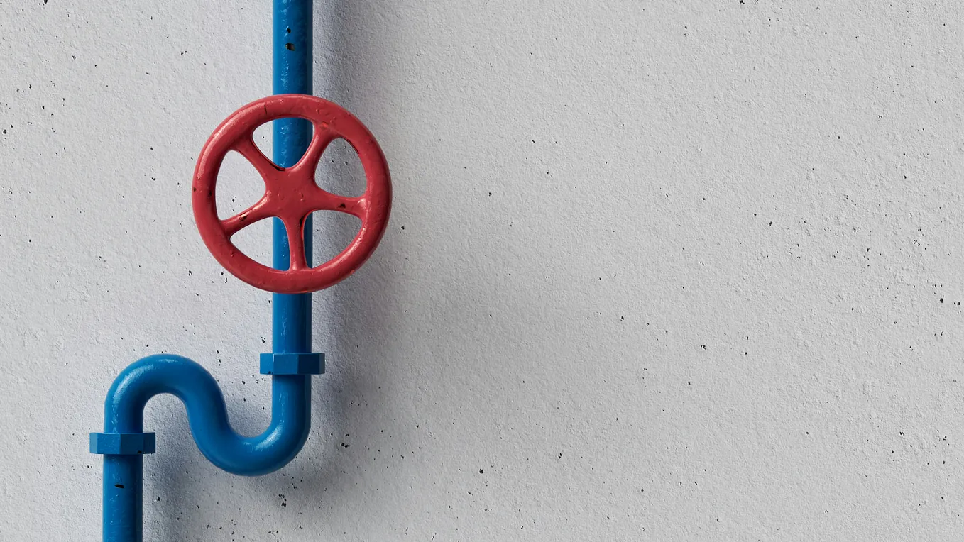 Clean blue piping and a red turn wheel that looks like old-fashioned steel manufacturing against a white-washed wall. Reminiscent of an American factory but without the hardknocks.