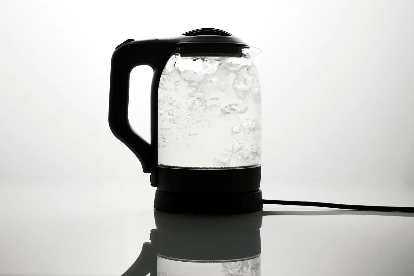 A transparent kettle with black plastic handle, lid and base, is filled with boiling water.