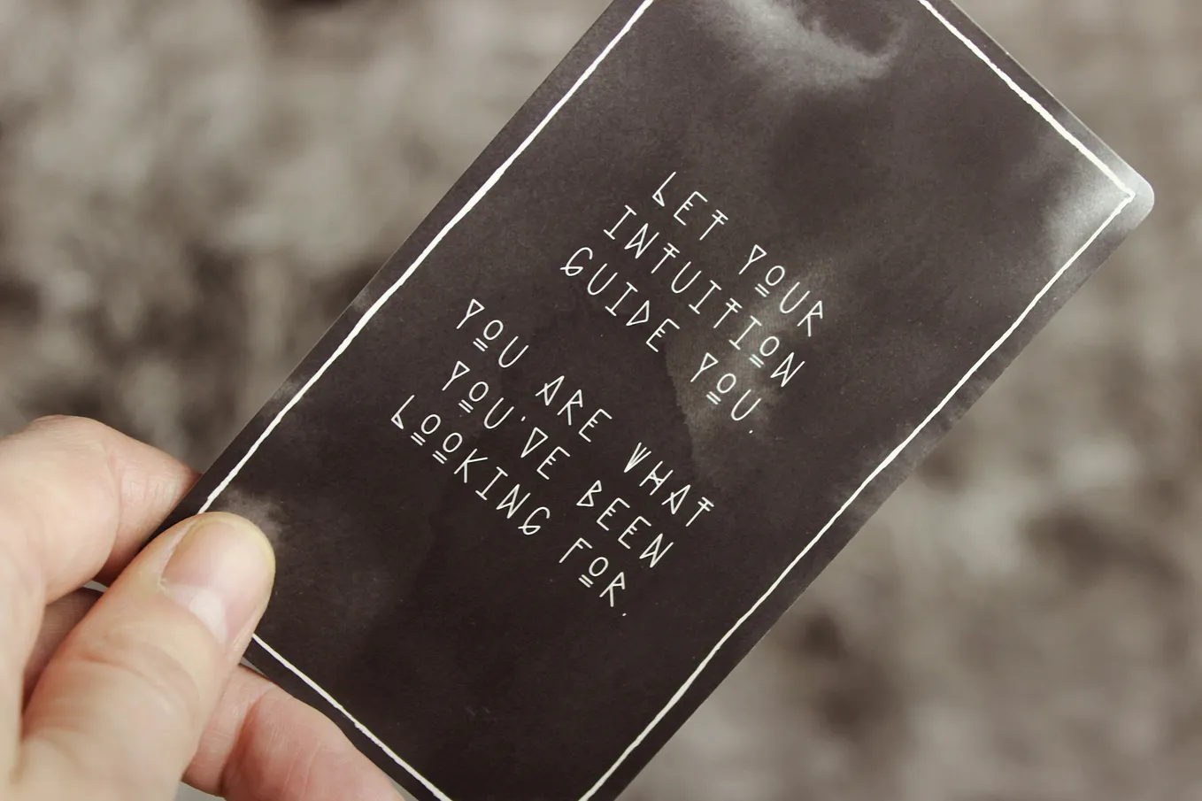 Black and white tarot card with message "let your intuition guide you, you are what you have been looking for" is displayed, held in a woman's hand.