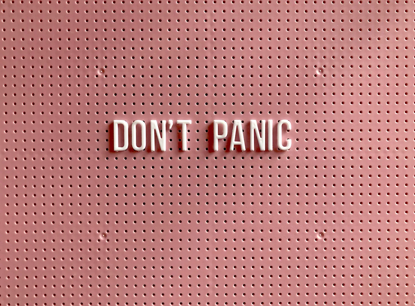All-caps letters spelling out “Don’t panic” in petal pink on a blush-colored cork board.
