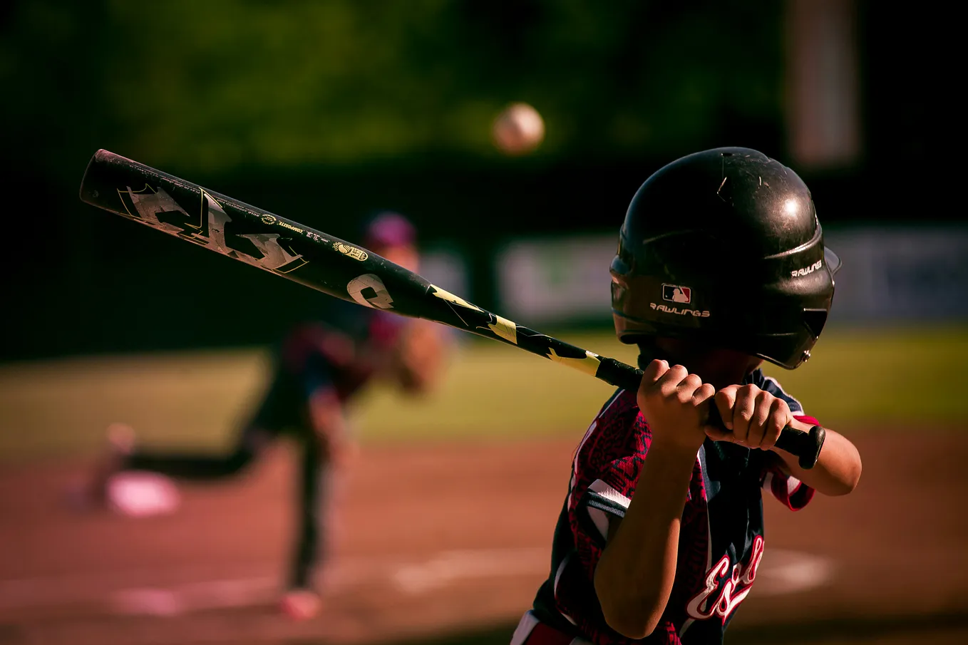 child holding a bat. Ball comes toward him. Baseball.