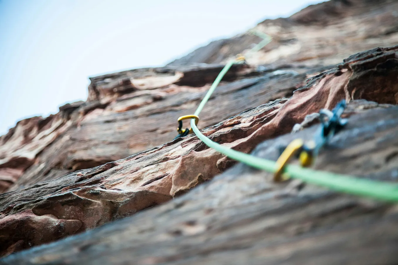 A rock wall with a green climbing rope attached to it by brackets