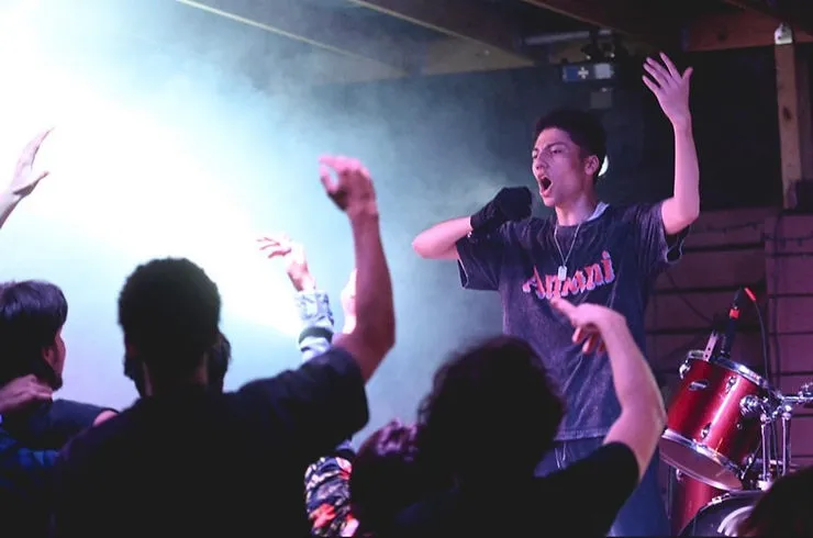 The Music Artist, Amani, performing his Hip-Hop Set in front of a large crowd wearing his gray “Amani” merch shirt.