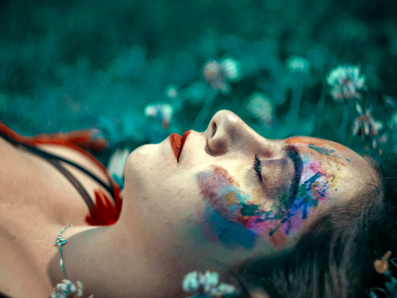 A freelancer lies on grass with eyes closed, colorful paint adorning their face. White flowers are scattered around, and the background is blurred. The scene exudes a serene, artistic atmosphere, capturing the essence of a solopreneur’s tranquil escape from failing systems.