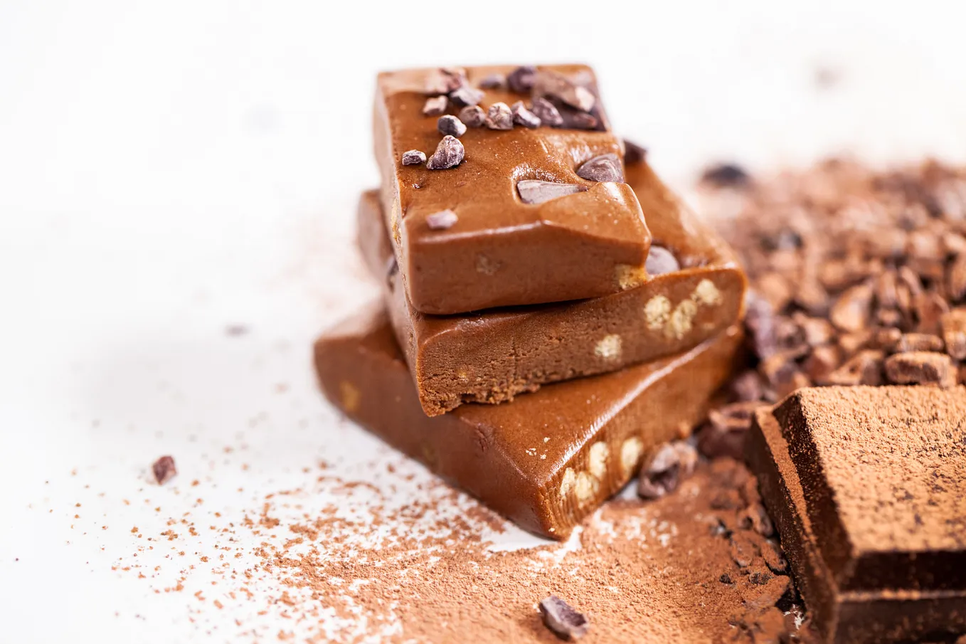 a chocolate protein bar cut into pieces and stacked, sitting on a white table dusted with cocoa powder and chocolate chips