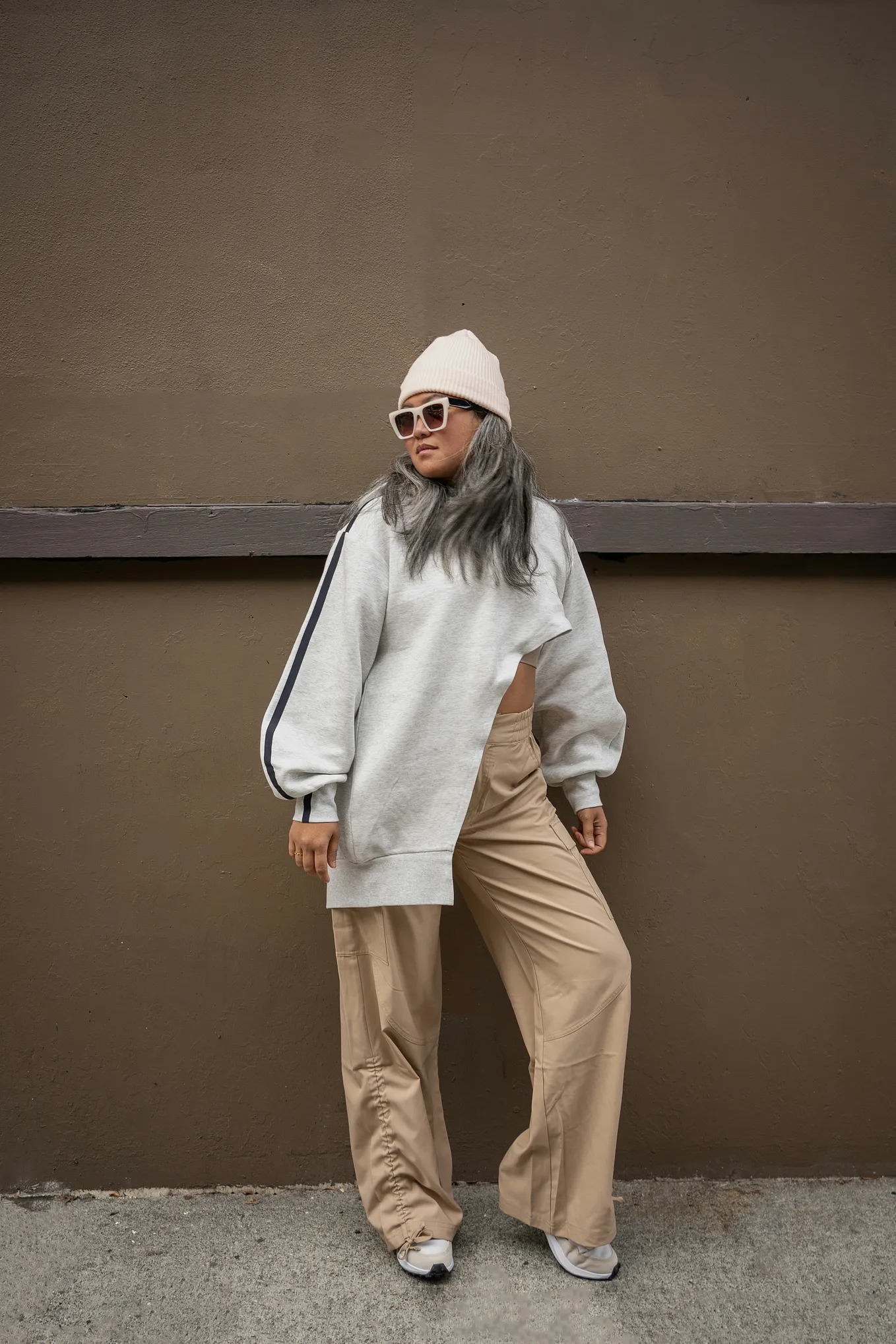 a woman wearing high fashion clothing, posing with sunglasses on and a winter hat, showing her long gray hair