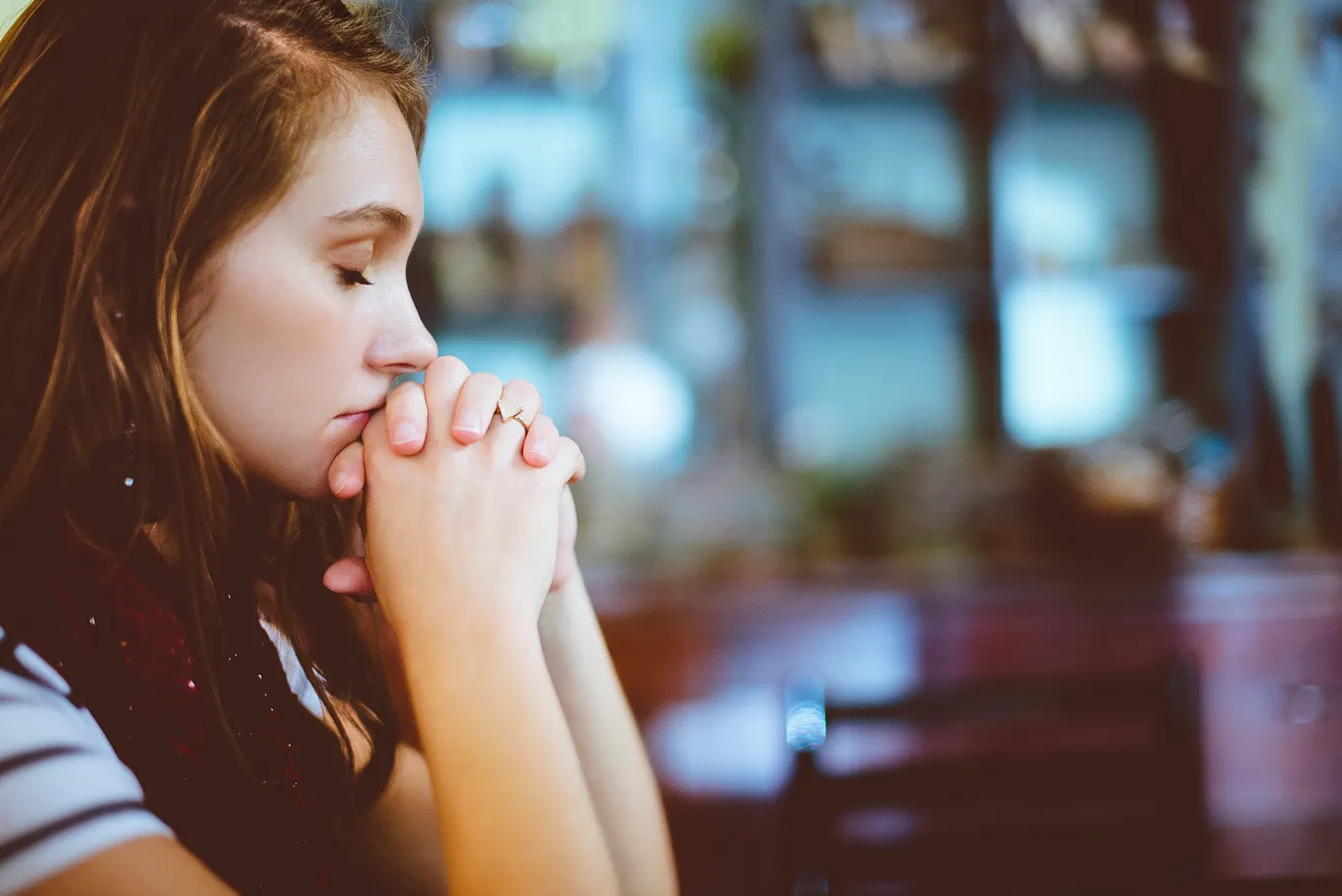 A young woman is praying with her fingers woven together and in front of her mouth. Her elbows seem to be on the altar.