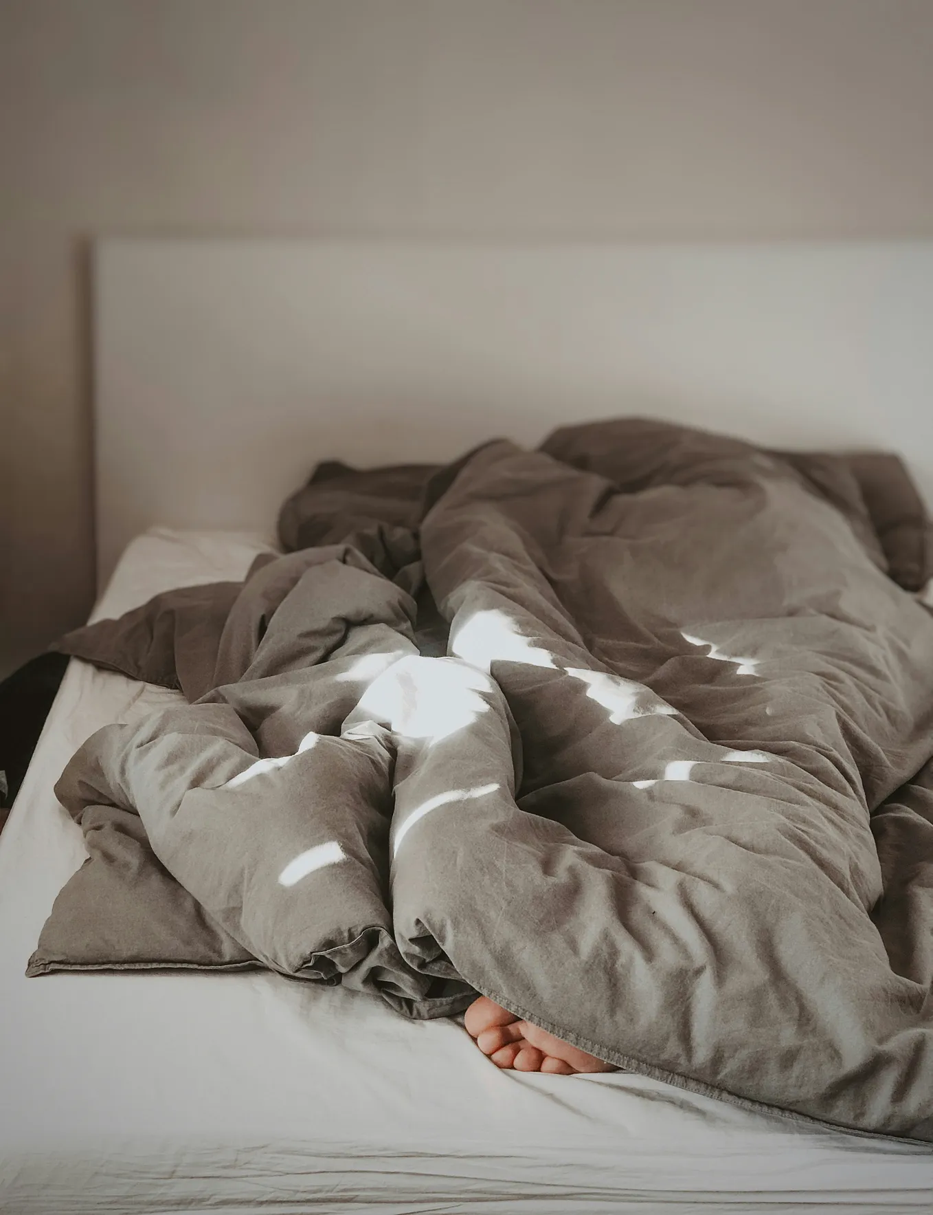 Comforter on top of an unmade bed, with a foot sticking out of the end