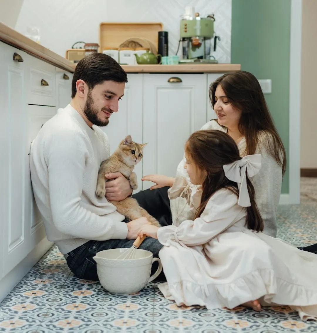 A family holding a cat and mixing dinner on the kitchen floor.