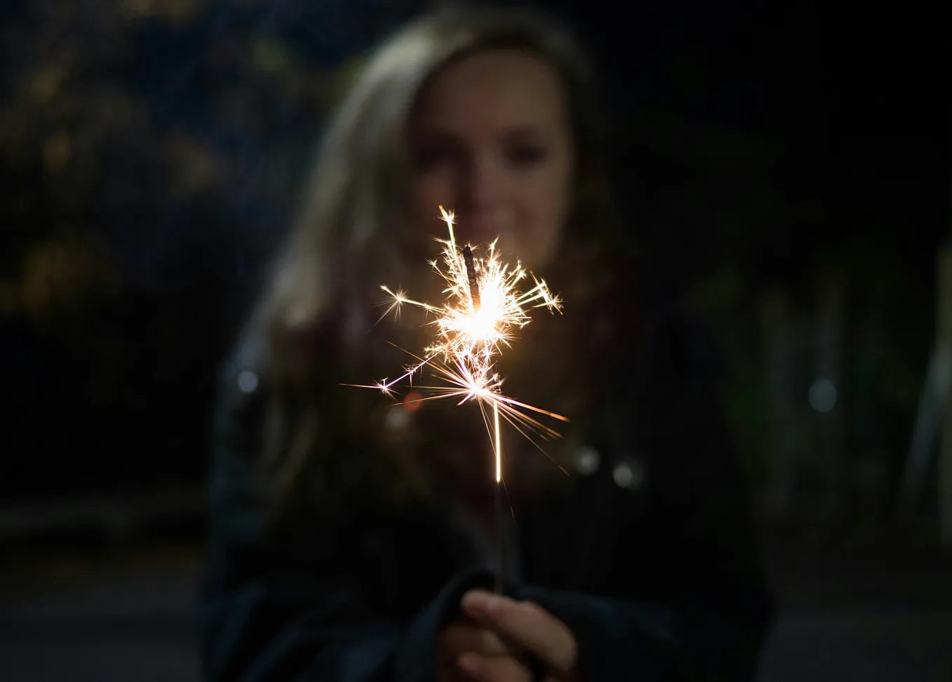 A sparkler held forward by a woman out of focus.