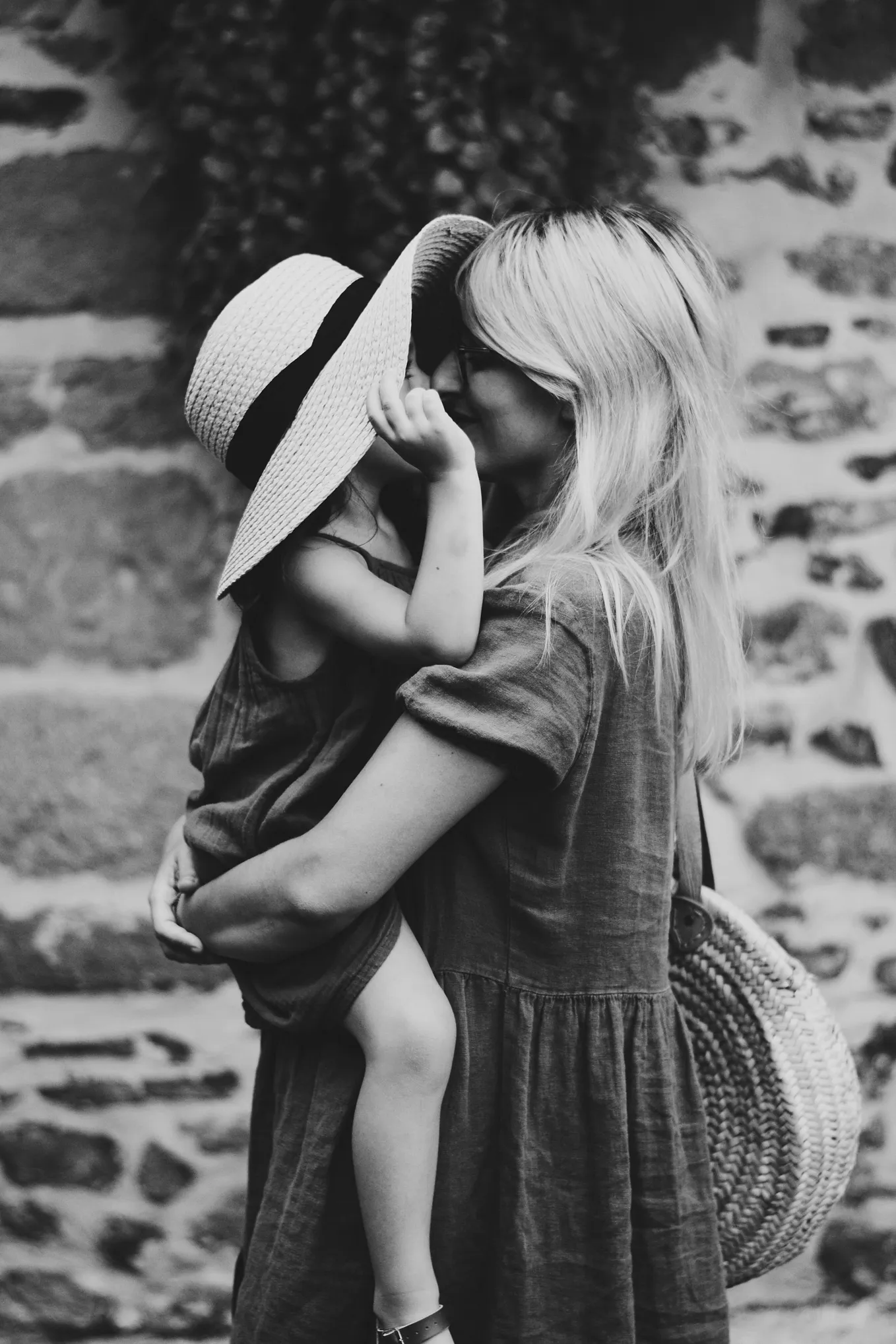 Mother holding her daughter in her arms, tenderly kissing her under her hat.