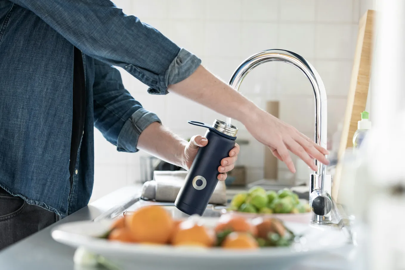 A picture of someone filling a water bottle at a kitchen faucet.