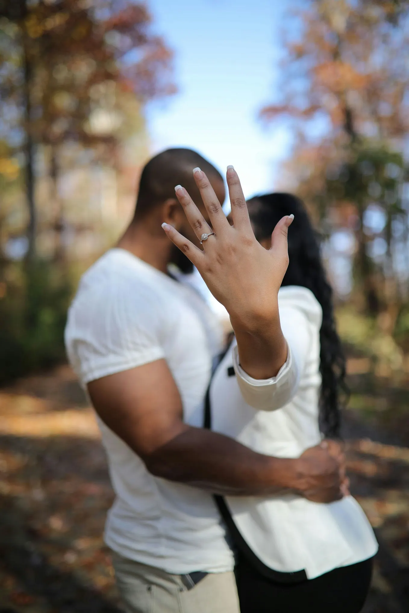A young woman kissing a young man holds her hand up in front of her face. There is a ring on her hand.