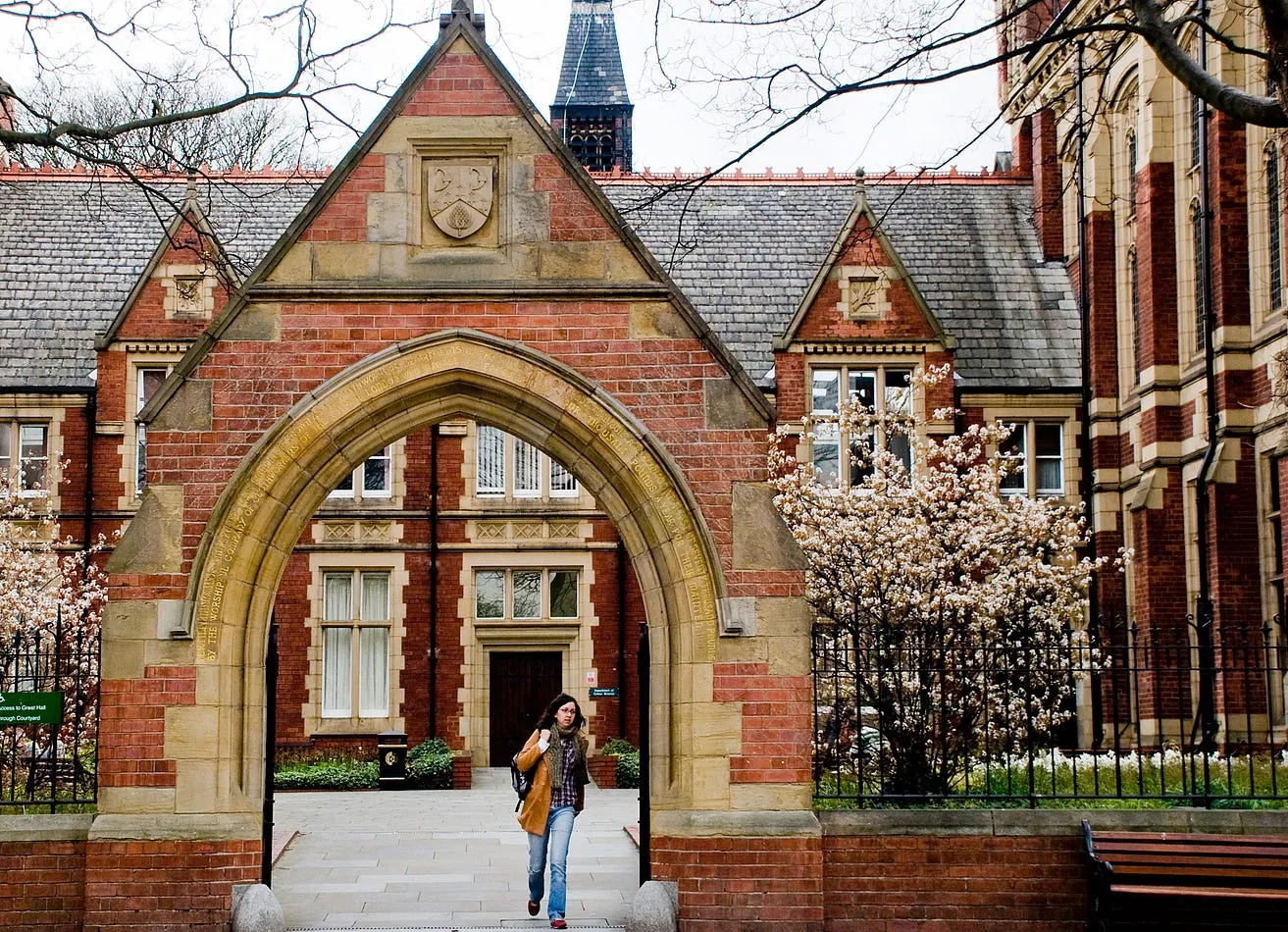 A person stands under the distinctive Clothworkers Arch. A triangular arch with red and yellow brick and black railings either side.