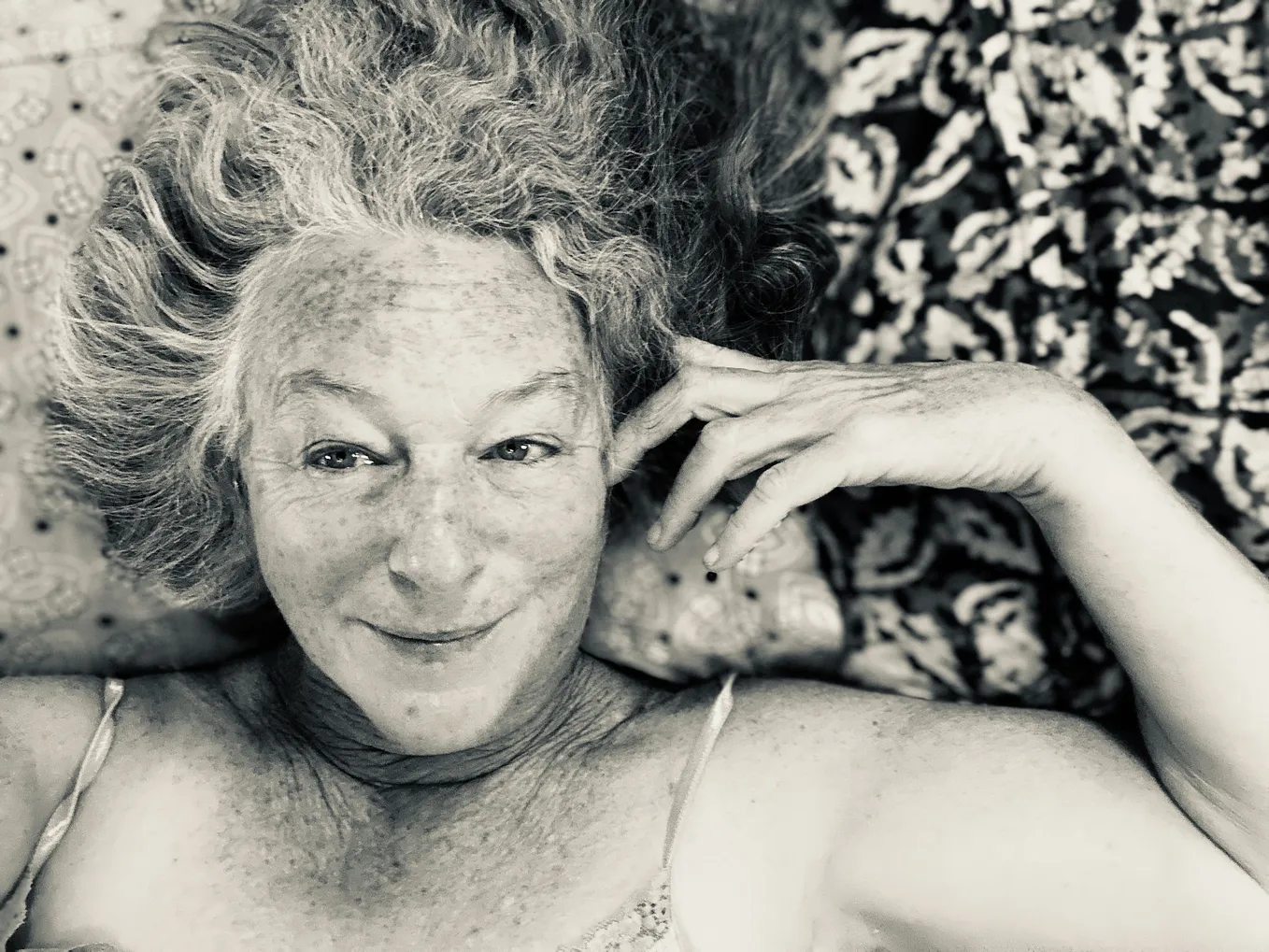 A black and white photo of an older woman lying on a bed. Just head and shoulders are showing