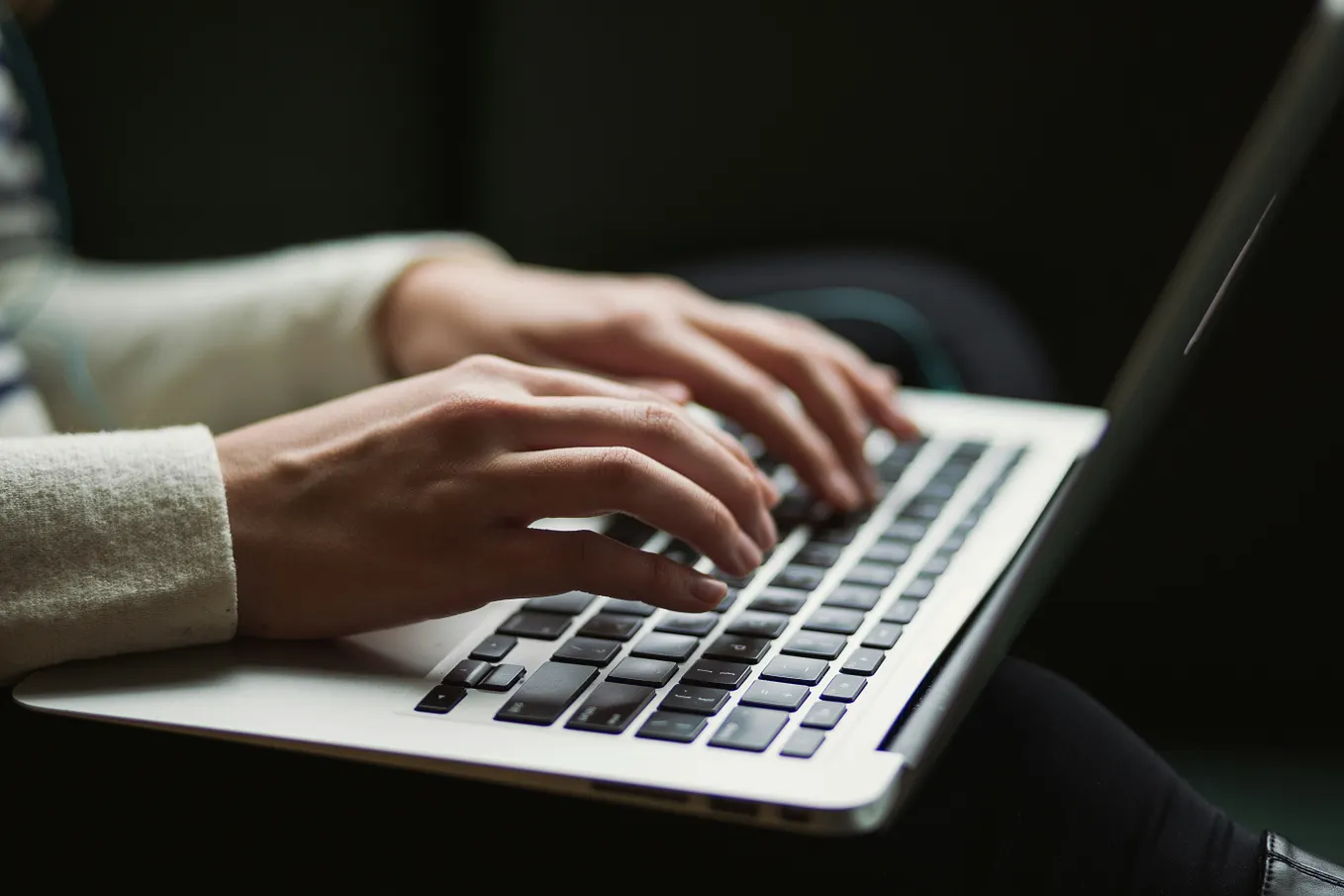 Color photo of two hands typing on a laptop keyboard.