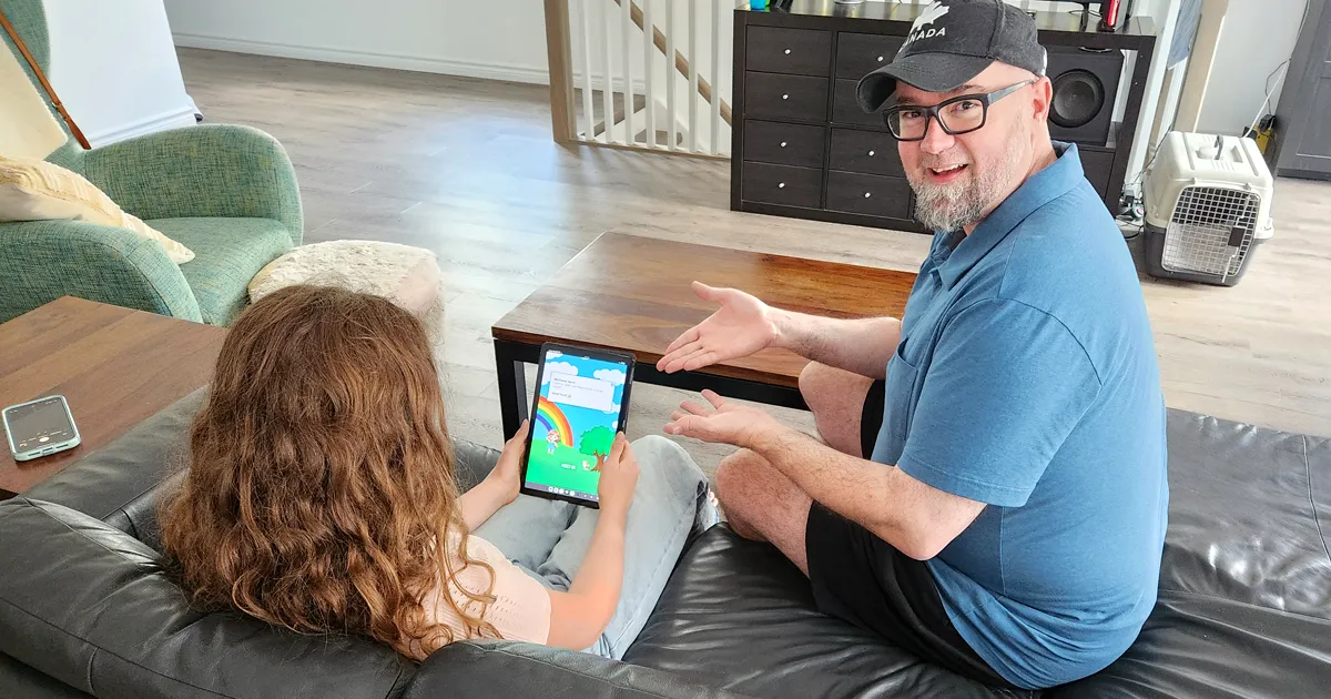 Father sitting beside daughter who is playing a mobile game on a tablet