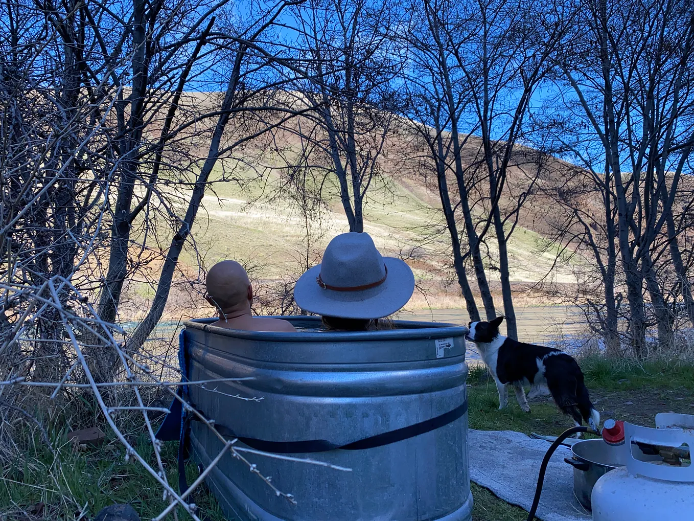 Author and girlfriend sitting in metal tank hot tub looking out at river.
