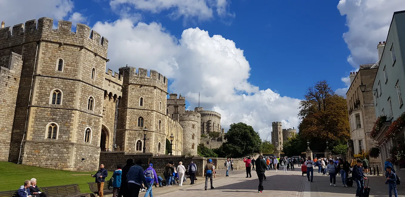 Castle walls with road past full of people mulling about on a bright sunny day with blue sky and fluffy white clouds