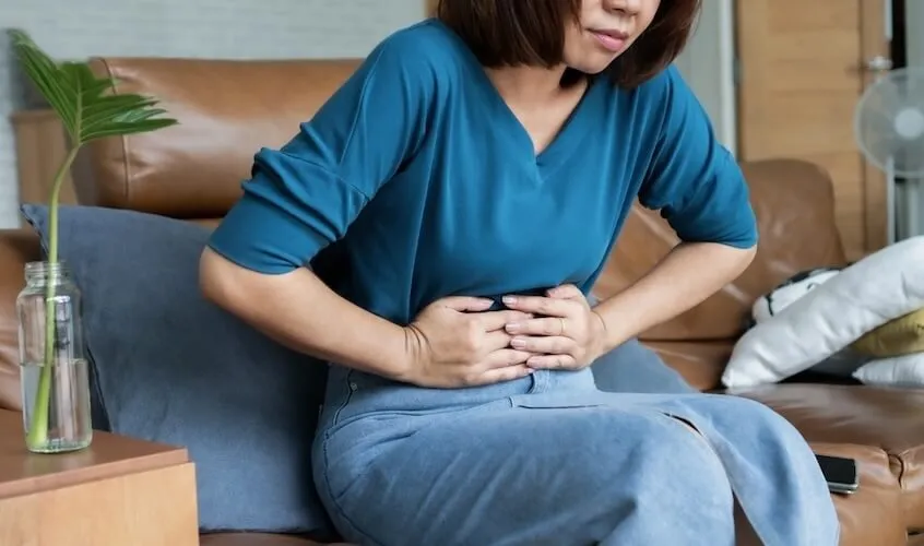 Asian woman with hands on her stomach feeling IBS pain