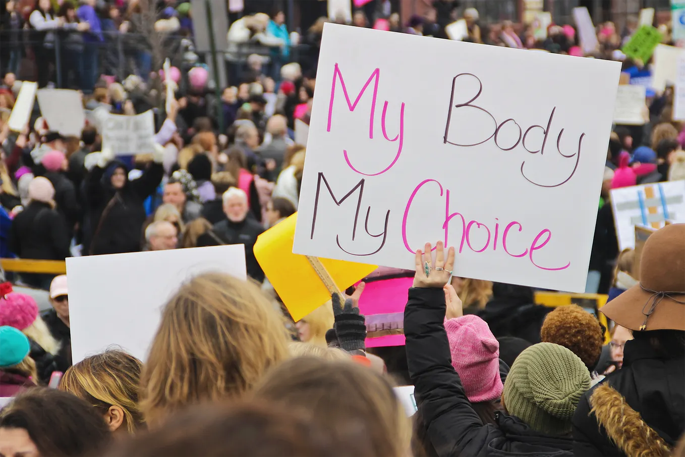 A group of people in a protest, including one woman holding a sign that says “My Body My Choice”