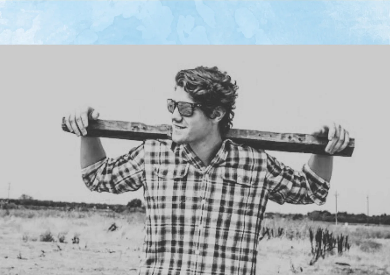 A young man with a post along his shoulders, fields behind and a sky background above