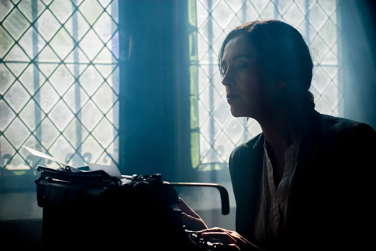 A woman peers at a typewriter with a troubled expression on her face, beside a window