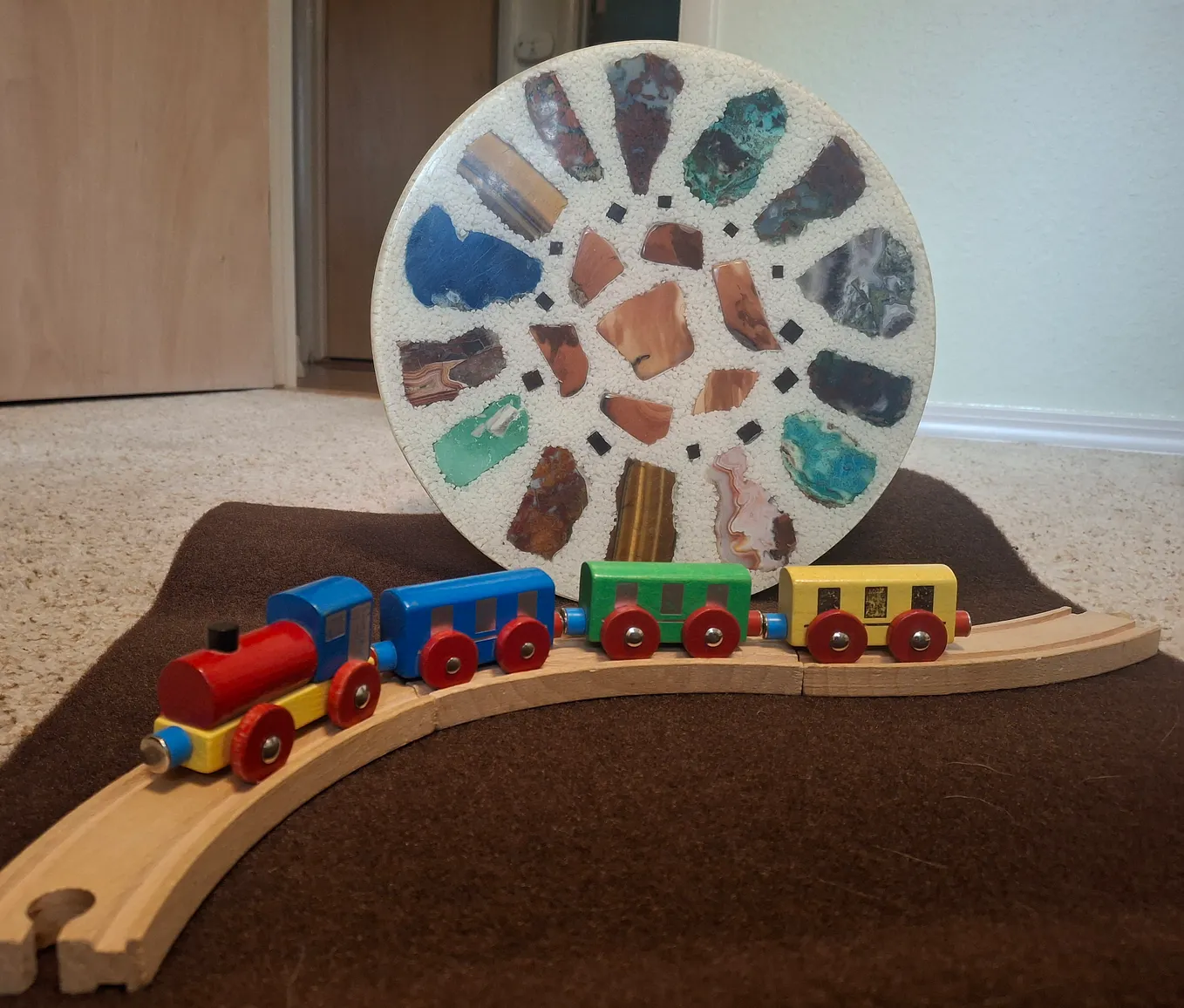 a toy train on wood track, table of set-in stones behind it.