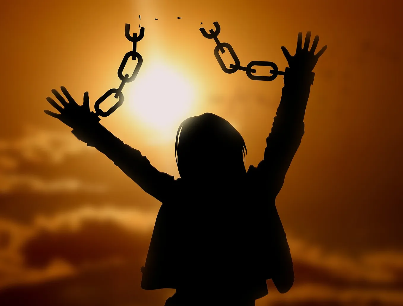 Raised hands and broken chain with sun and clouds in background