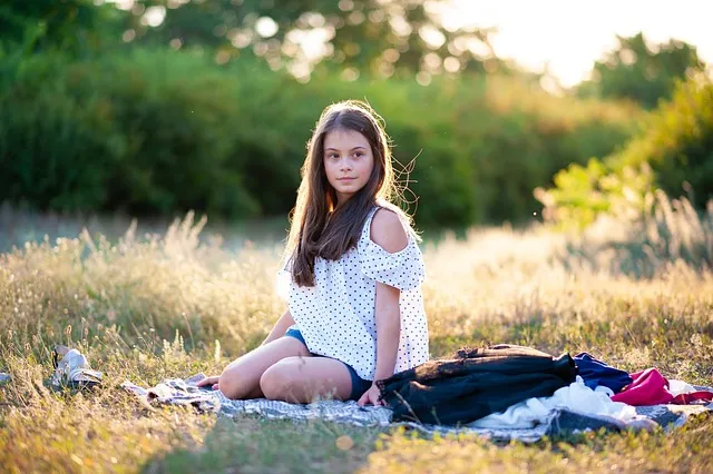 A preteen girl sitting on the grass near a pile of clothes