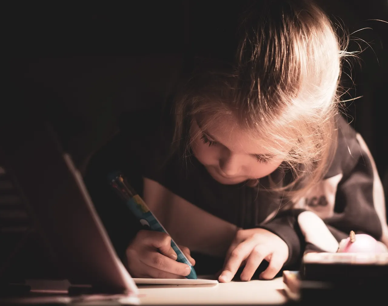 A young girl poised with a pen over a notebook, presumably completing her homework